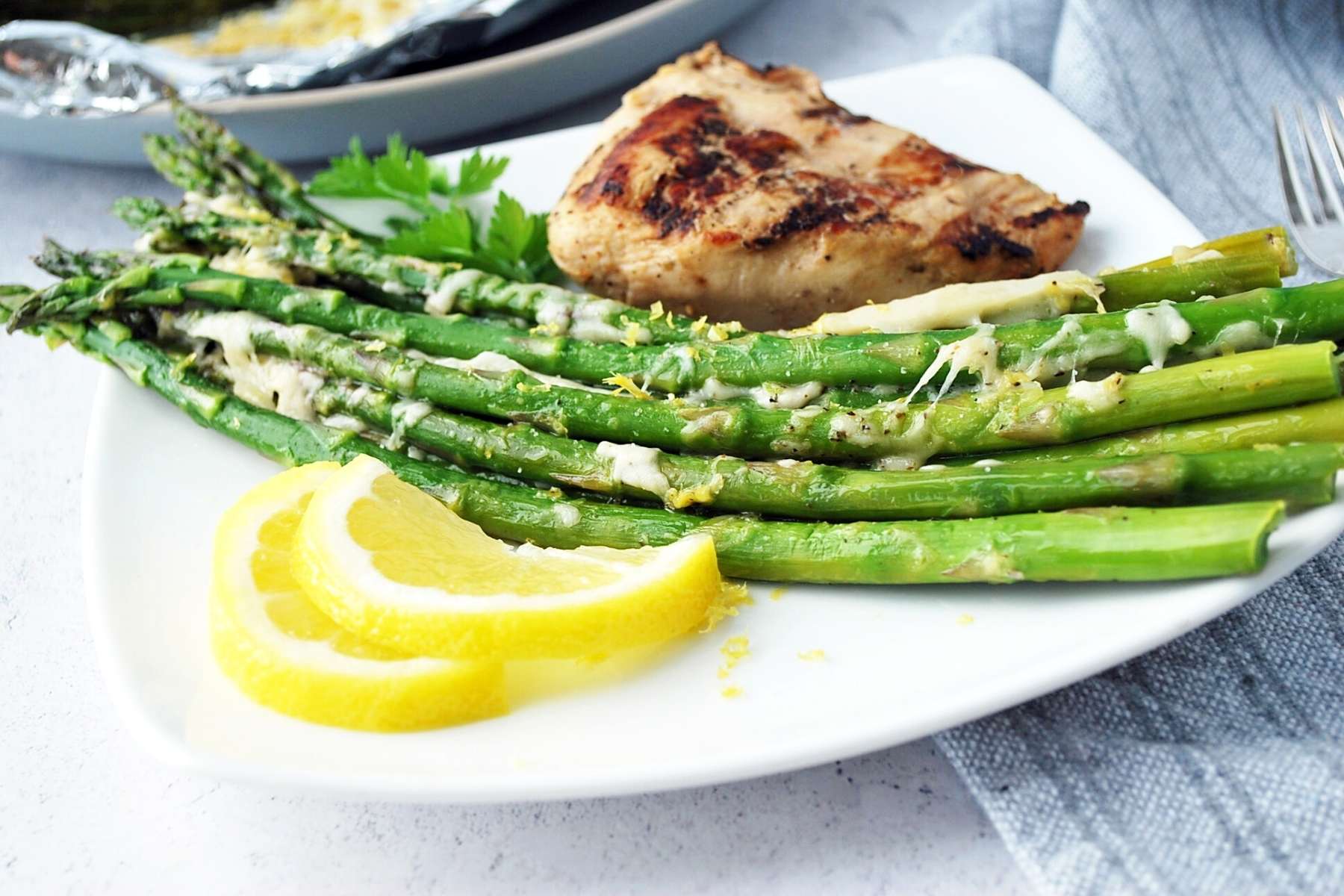Grilled asparagus on a plate with lemon slices and grilled chicken