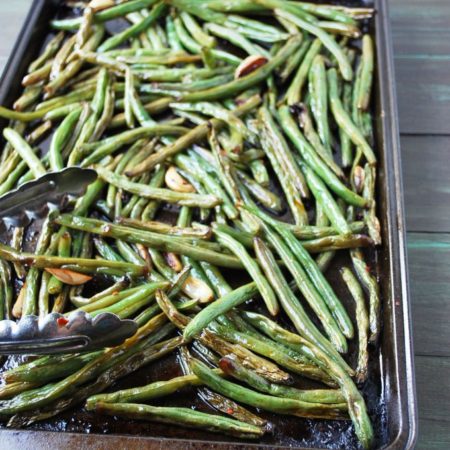 Roasted green beans on a cookie sheet with tongs