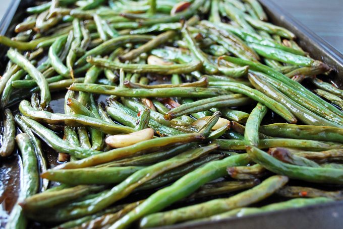 A close up of roasted green beans with garlic cloves