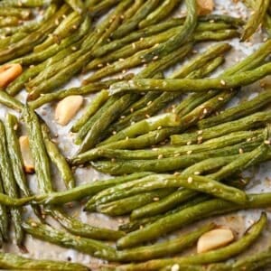 close up photo of green beans and whole garlic cloves roasted on a baking sheet