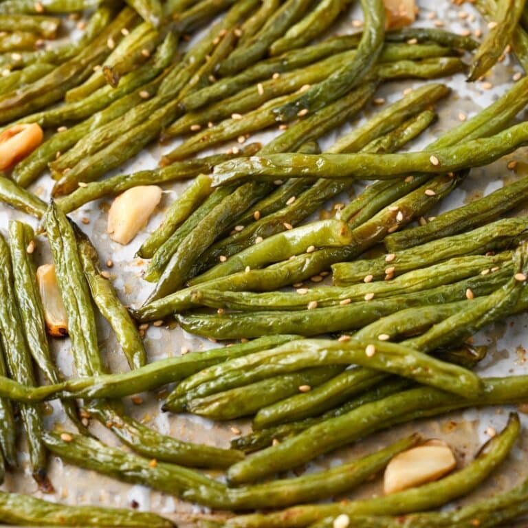 close up photo of green beans and whole garlic cloves roasted on a baking sheet