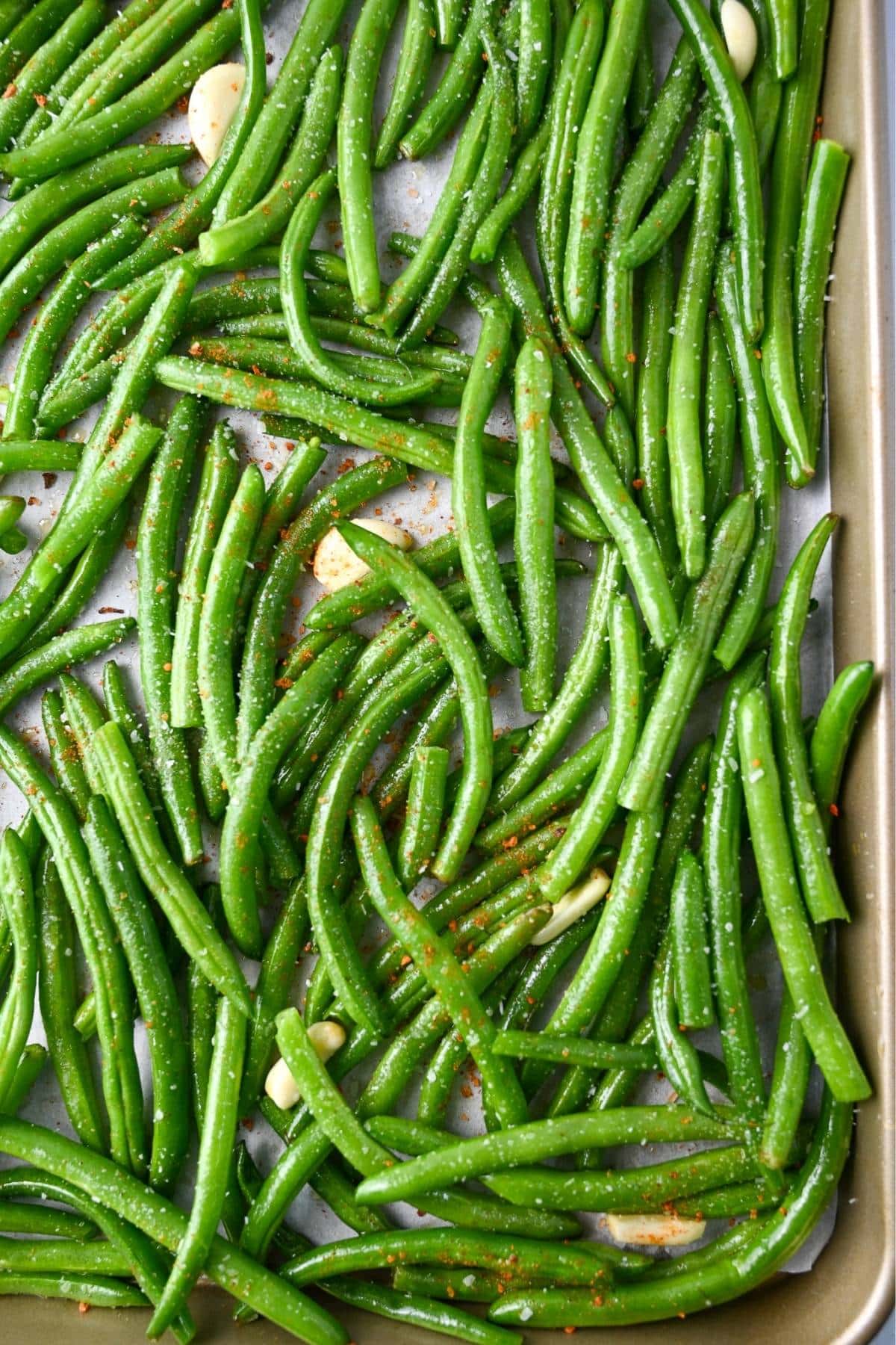 uncooked green beans with garlic, salt, olive oil and sriracha seasoning on a parchment lined baking sheet