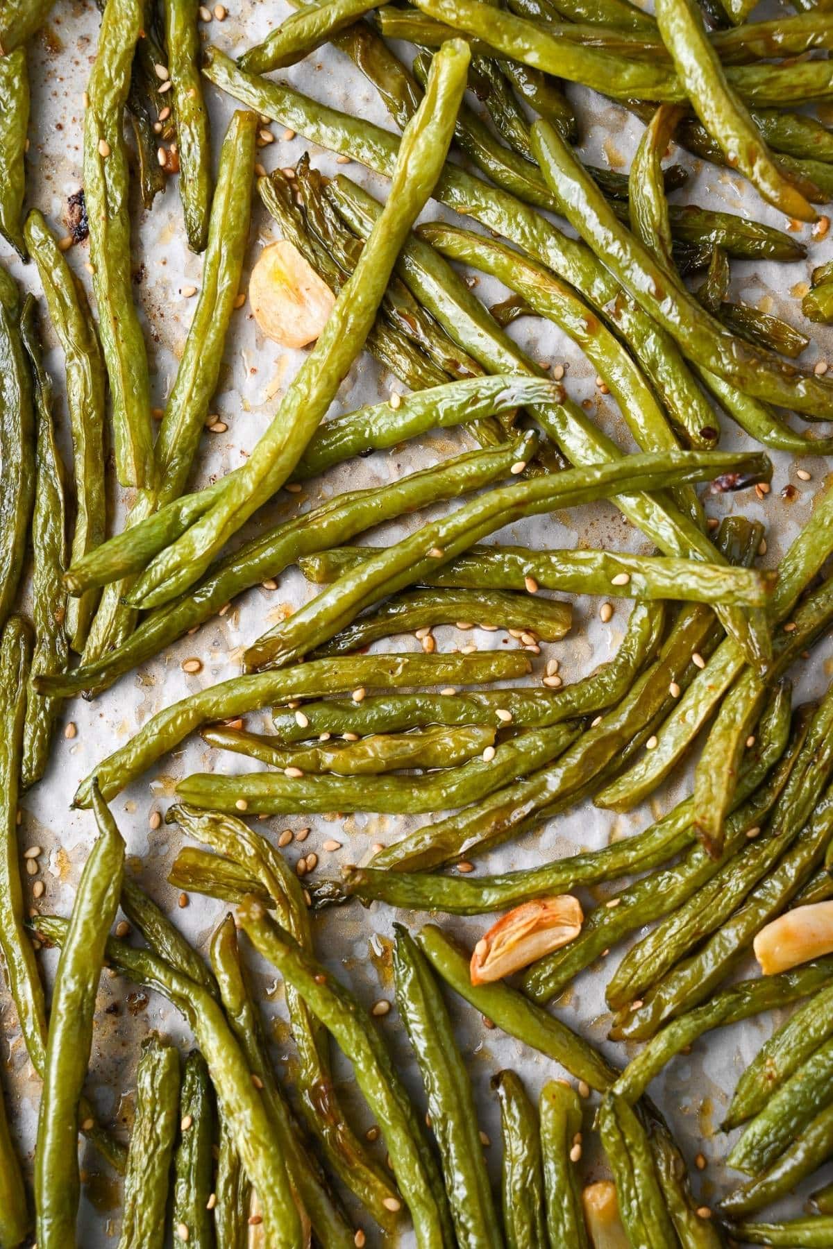 a baking sheet with roasted green beans and garlic sprinkled with roasted sesame seeds