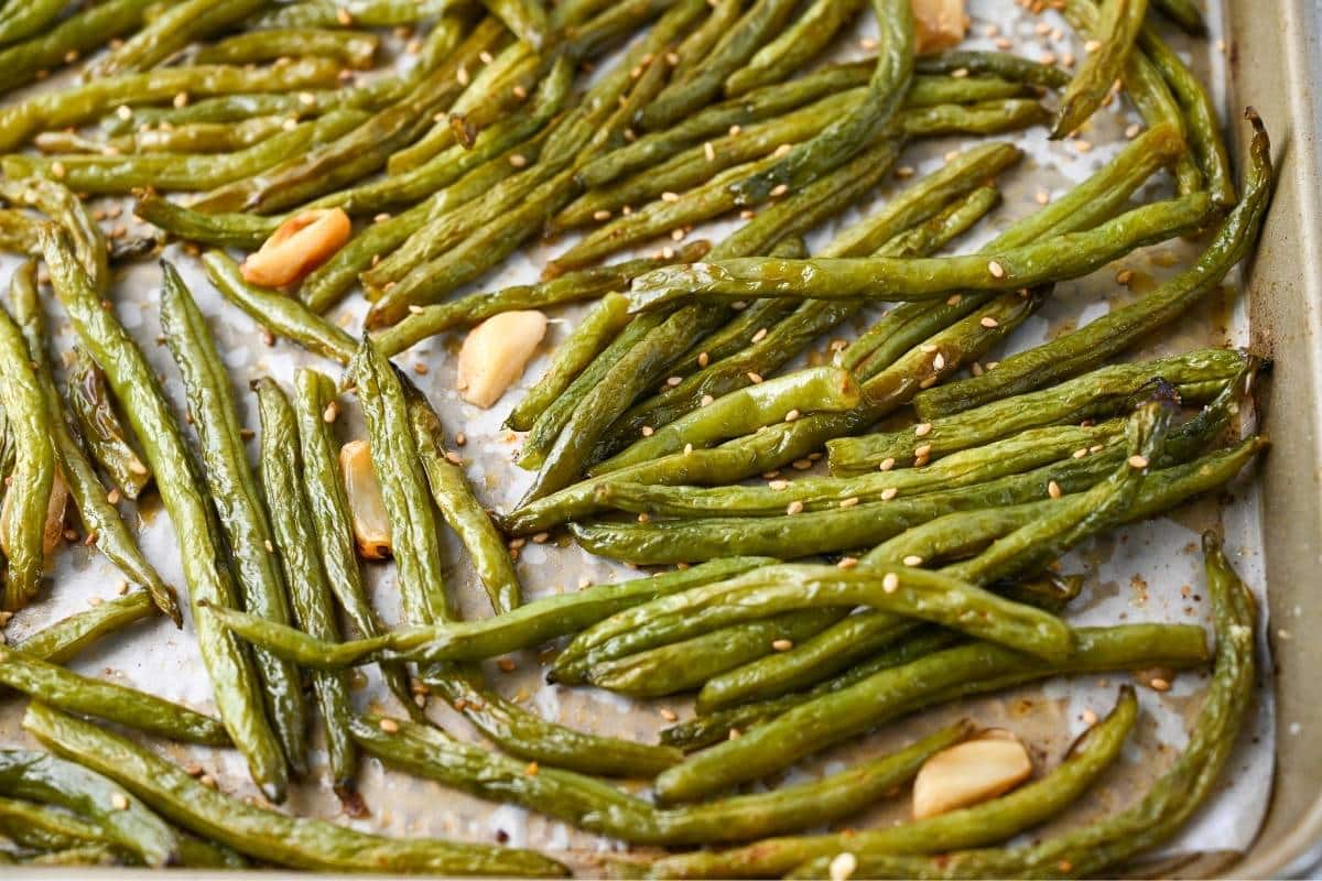 close up of green beans and garlic roasted on a baking sheet 