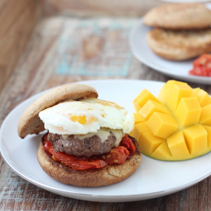 A breakfast sandwich on a plate with a sliced mango