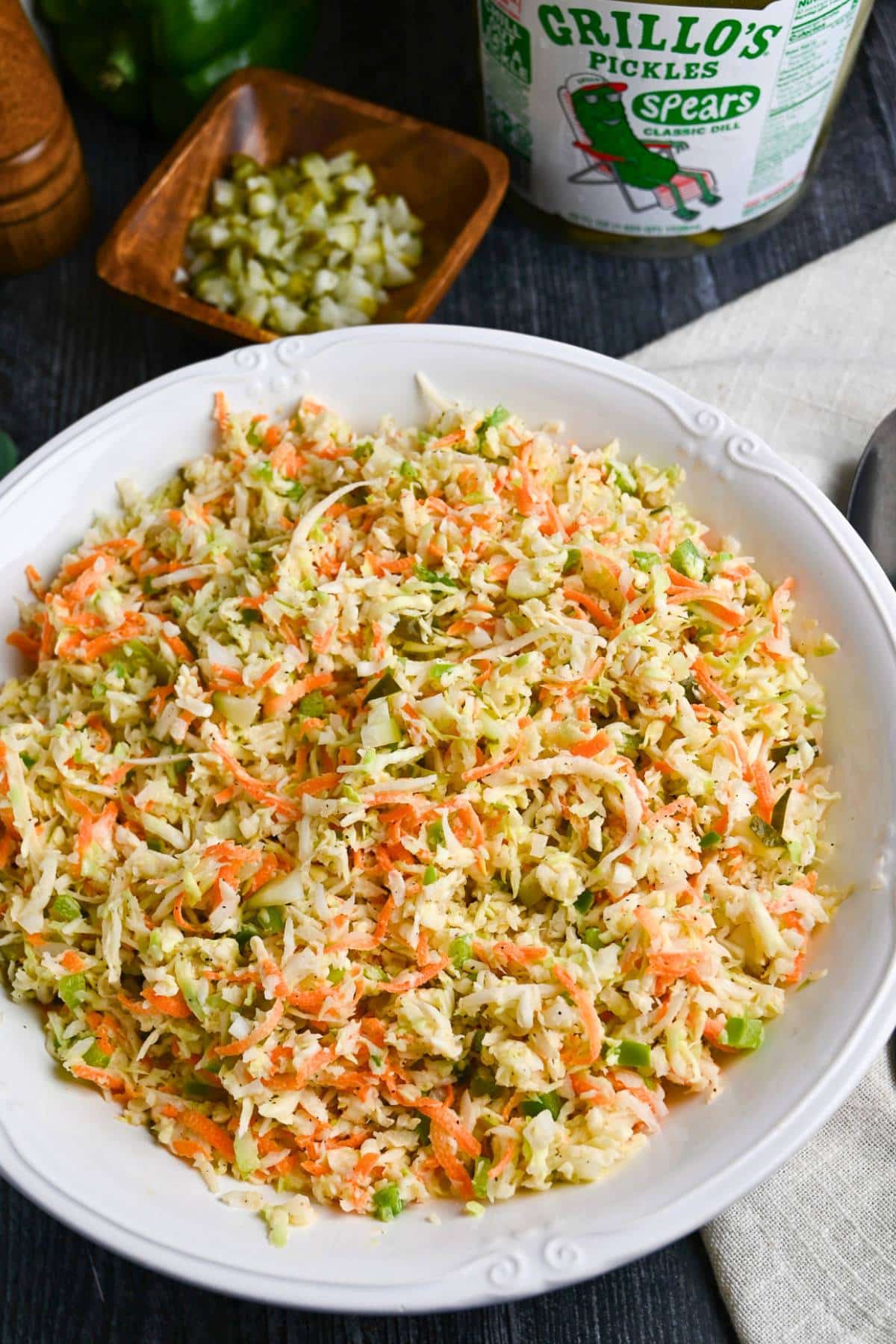close up of creamy vinegar slaw with dill pickles in a white bowl