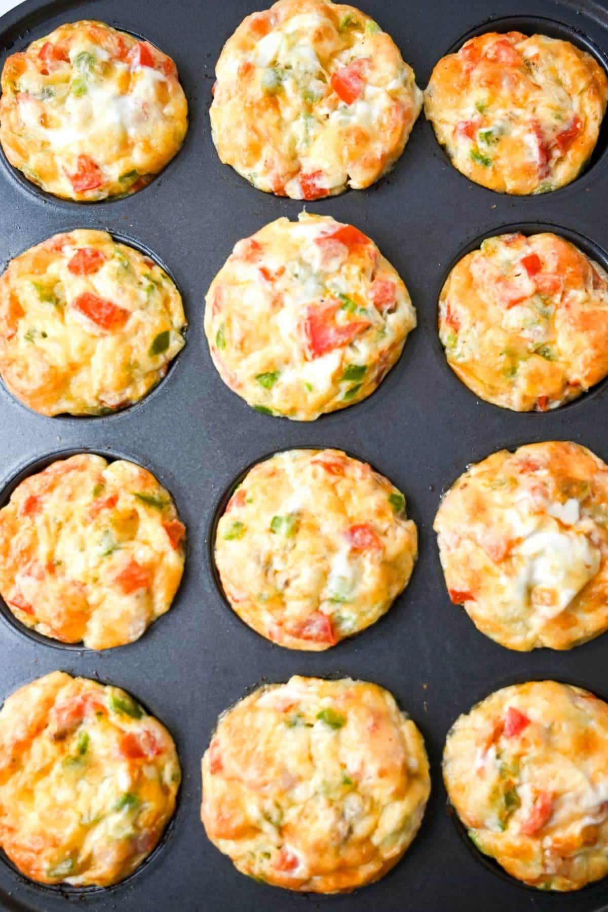 cooked egg muffins in a muffin tin with peppers, tomatoes, ground beef, and cheese