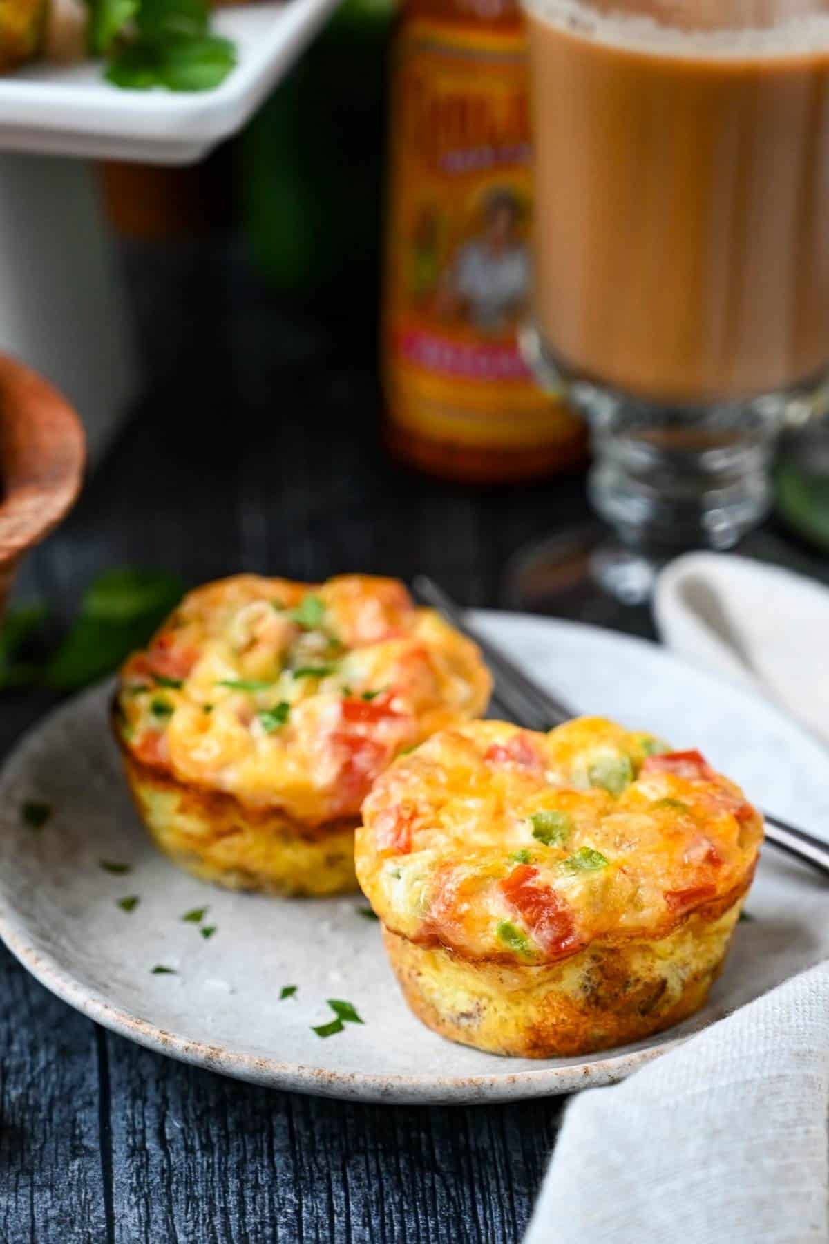 two southwest flavored egg muffins with ground beef on a plate with hot sauce and coffee in the background