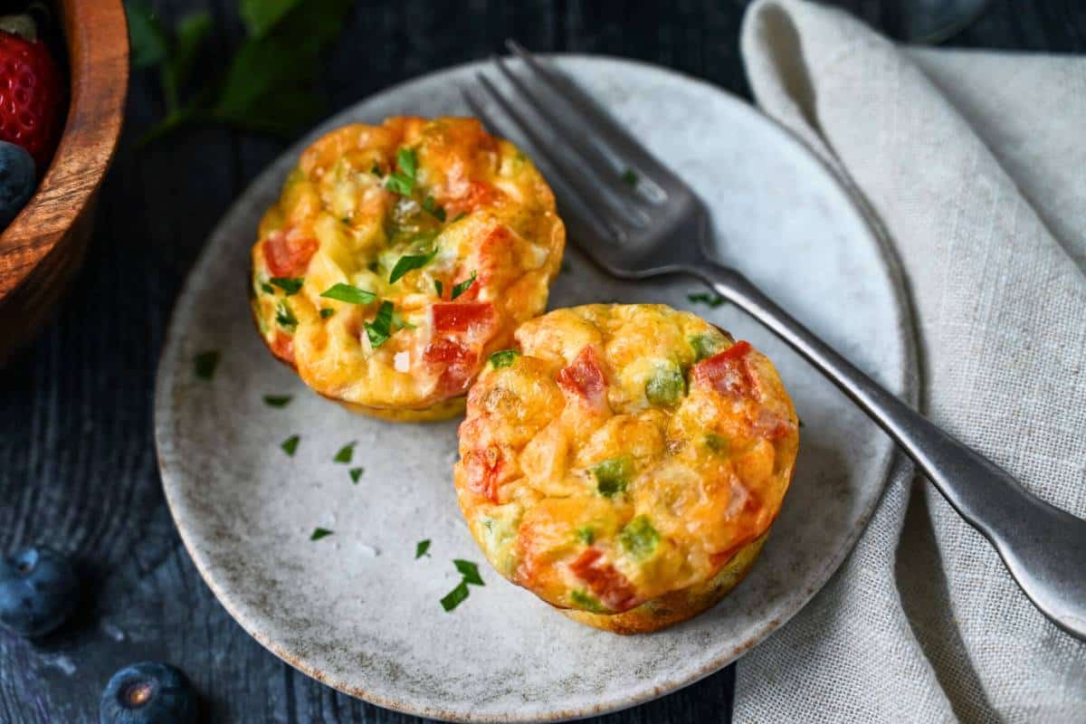 two egg muffins on a plate with a fork and fresh parsley