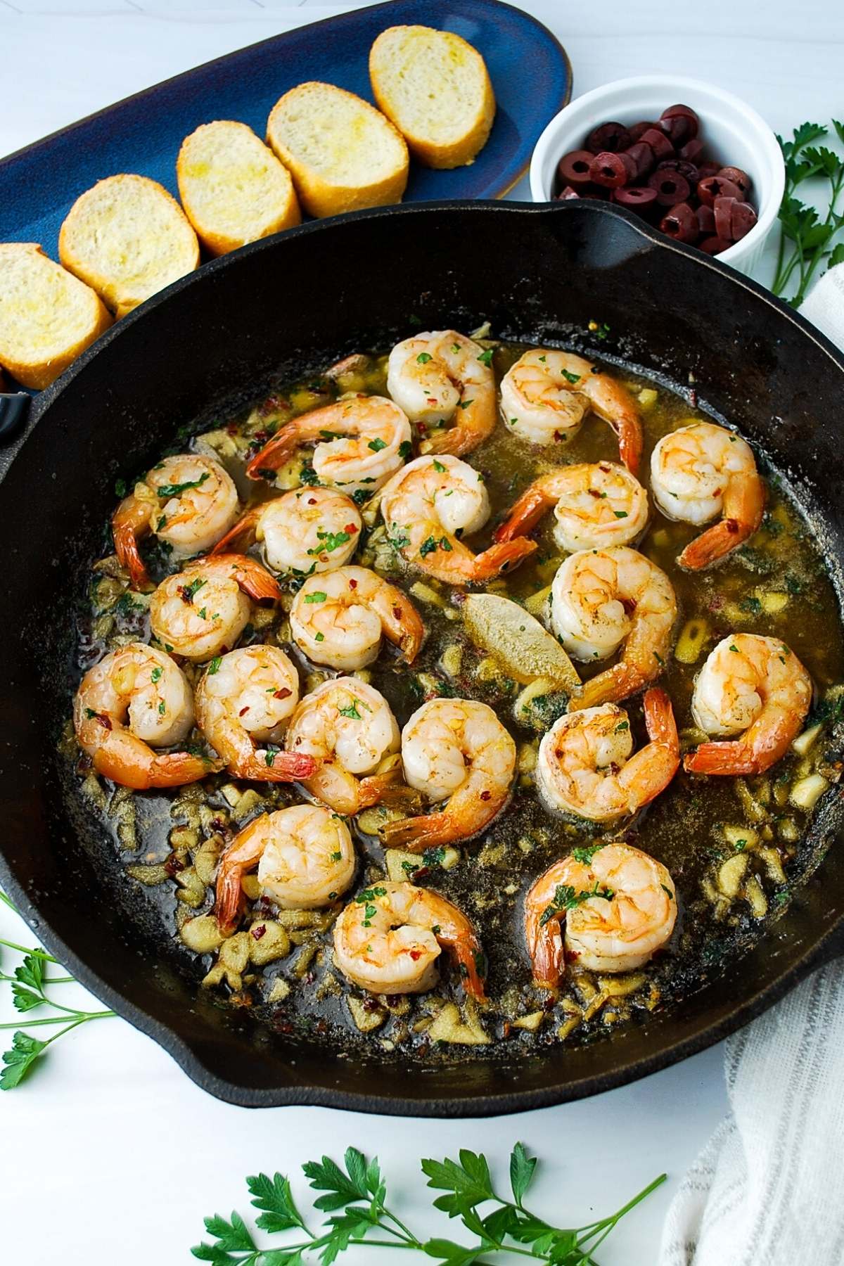 spanish prawns with garlic in a cast iron skillet with a tray of sliced bread and olives