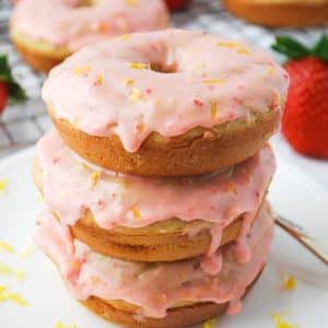 stack of frosted strawberry donuts with a rack of donuts in the background