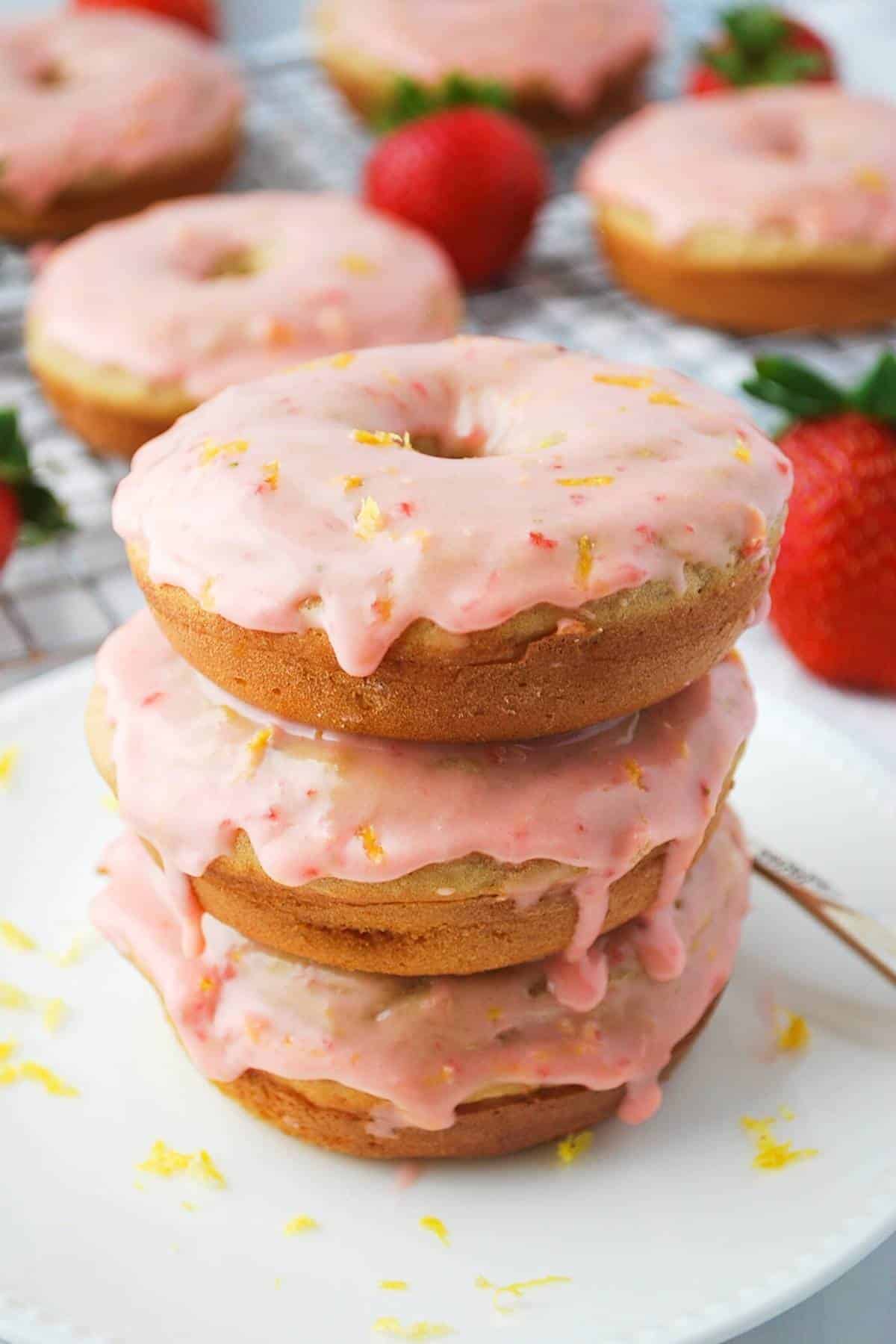 a stack of three frosted strawberry baked donuts with glaze dripping down the sides