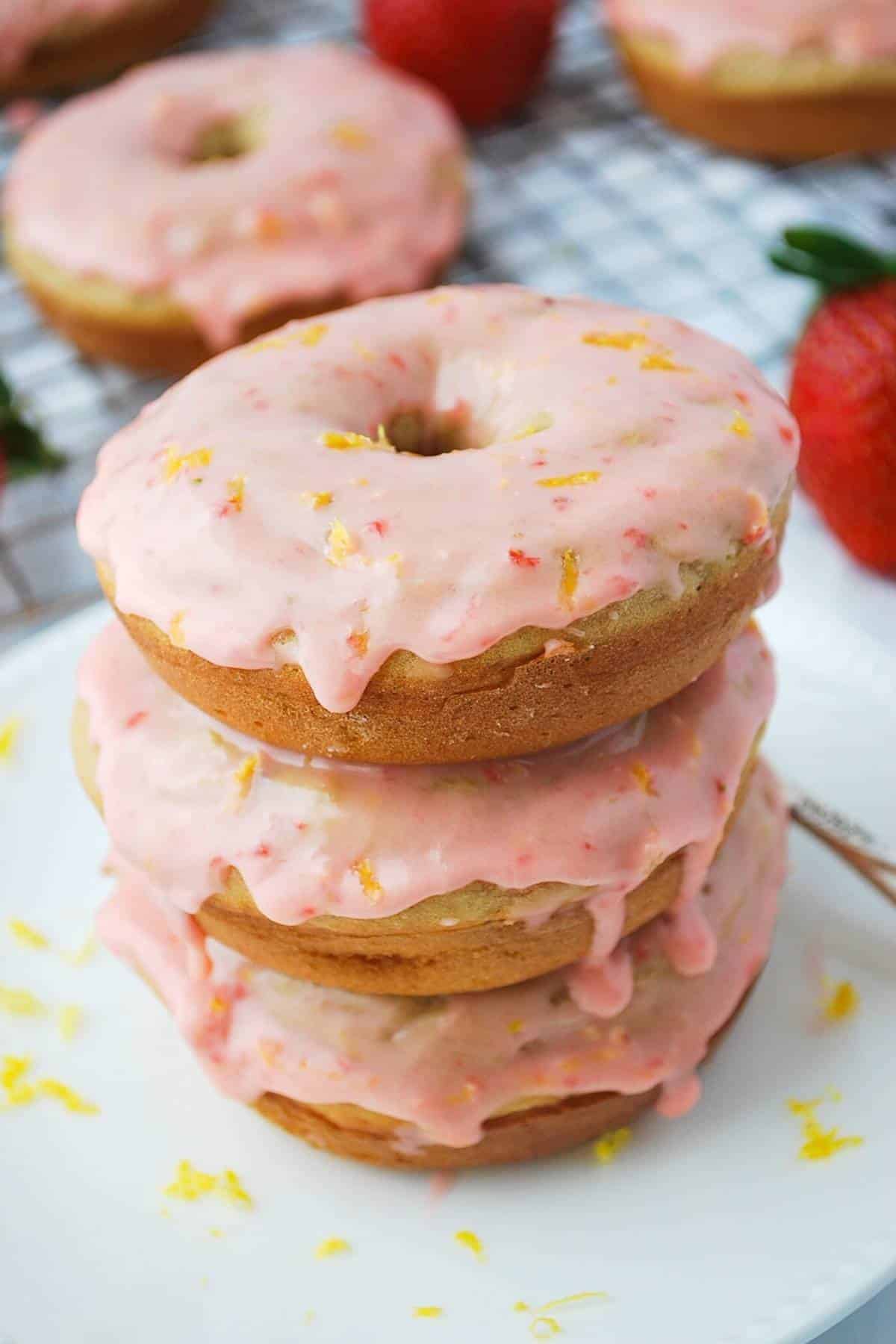 frosted strawberry donuts with fresh strawberries and a rack of donuts in the background