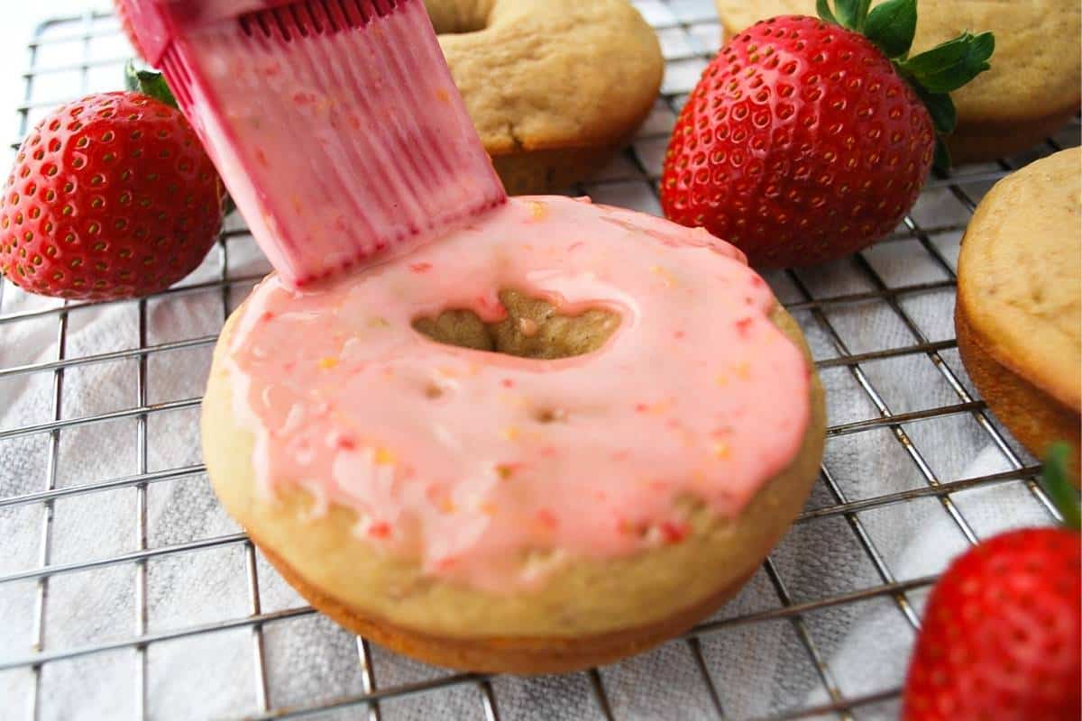 using a pastry brush to coat the top of a baked donut with glaze