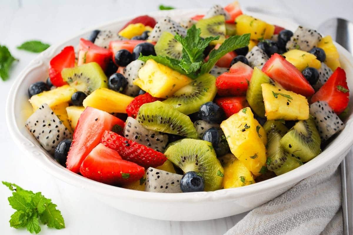 side view of a bowl of dragon fruit salad with pineapple, kiwi, summer berries and fresh mint with fresh mint around the bowl