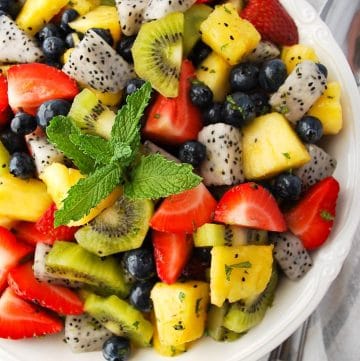 close up of dragon fruit salad in a white bowl topped with fresh mint