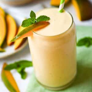 a mango shake in a glass with a sprig of mint and slice of mango on a green napkin