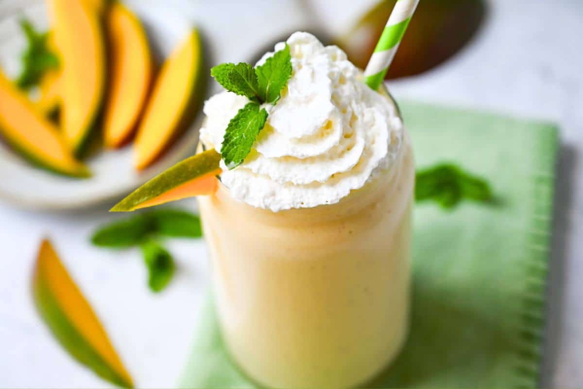 a healthy high protein mango shake with whipped cream on top with mint and a fresh mango slice