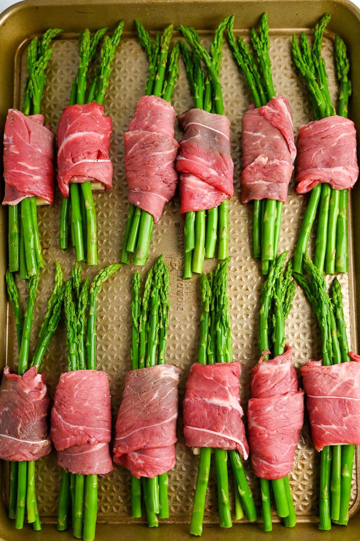 rolled up steak and asparagus on a baking sheet