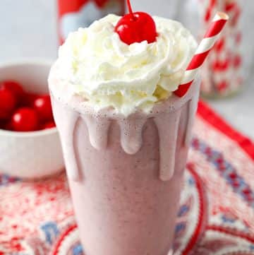 close up of a drippy cherry milkshake with whipped cream and a cherry on top with a red striped straw