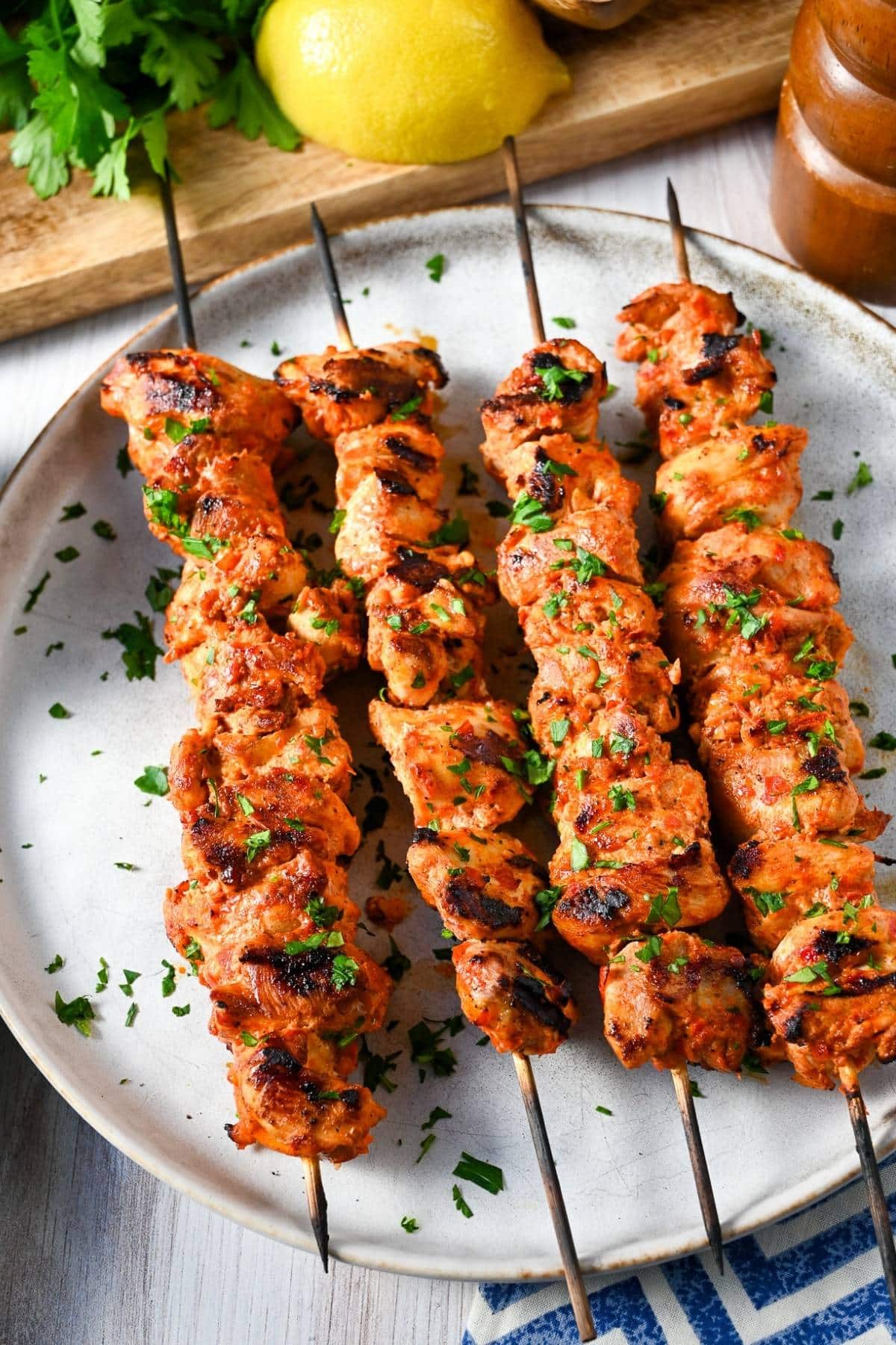 grilled chicken kabobs on a plate garnished with fresh parsley with a peppermill, lemon, and a napkin underneath