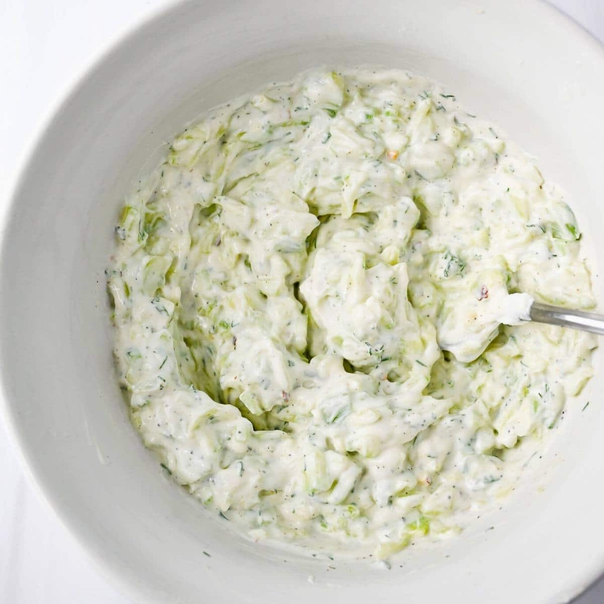 tzatziki sauce mixed in a white bowl with a spoon