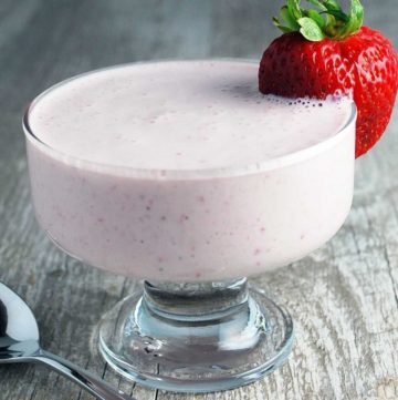 close up photo of strawberry yogurt in a parfait glass with a strawberry on the rim
