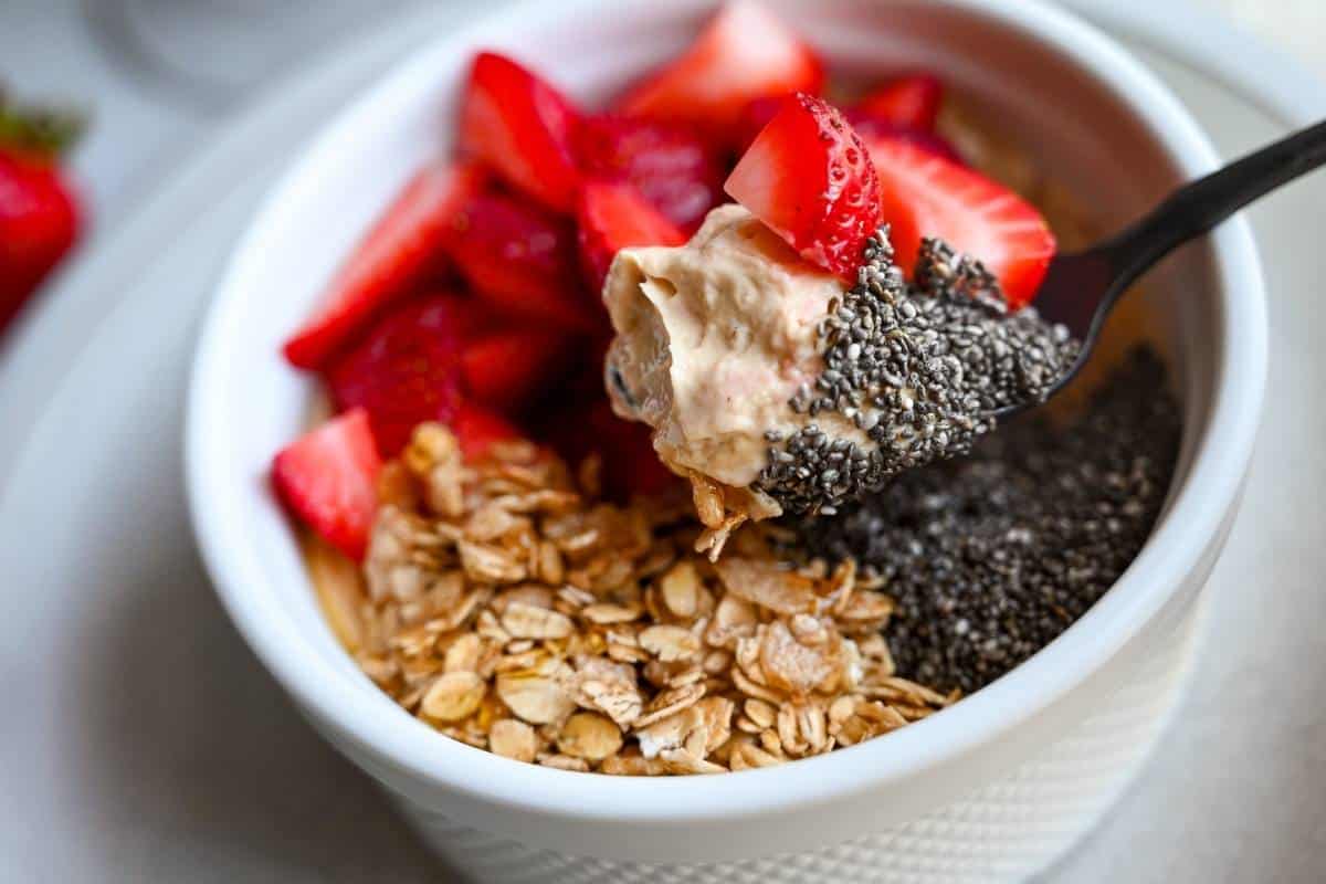 a spoonful of high protein yogurt mixed with peanut butter powder and topped with chia seeds, berries, and granola