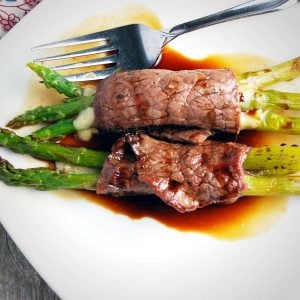 two beef asparagus bundles on a white plate drizzled in balsamic sauce