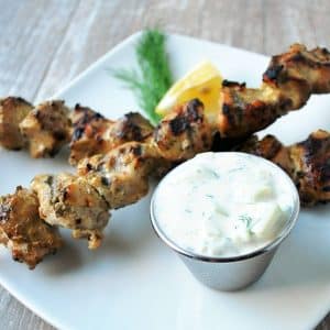 two yogurt marinated chicken skewers grilled and served on a white plate with tzatziki sauce