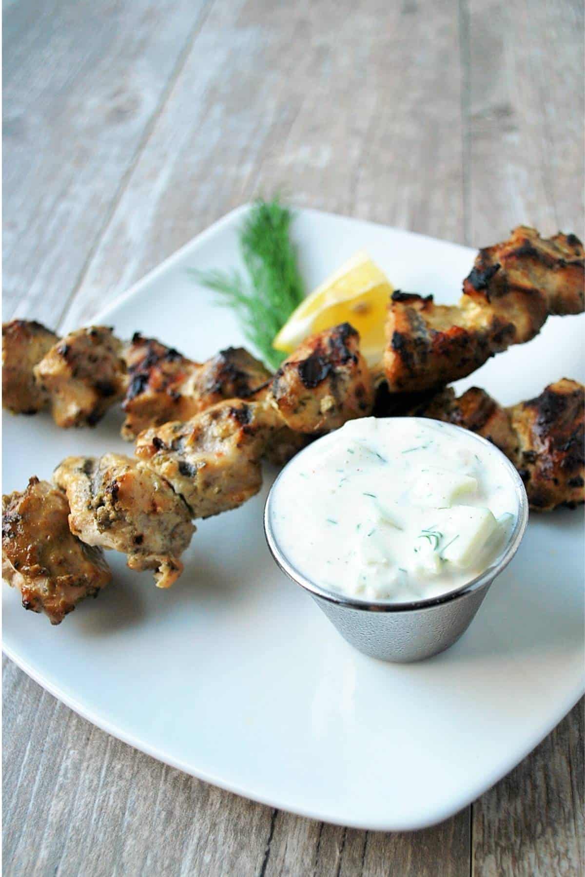 two grilled marinated chicken skewers plated with dill and lemon garnish