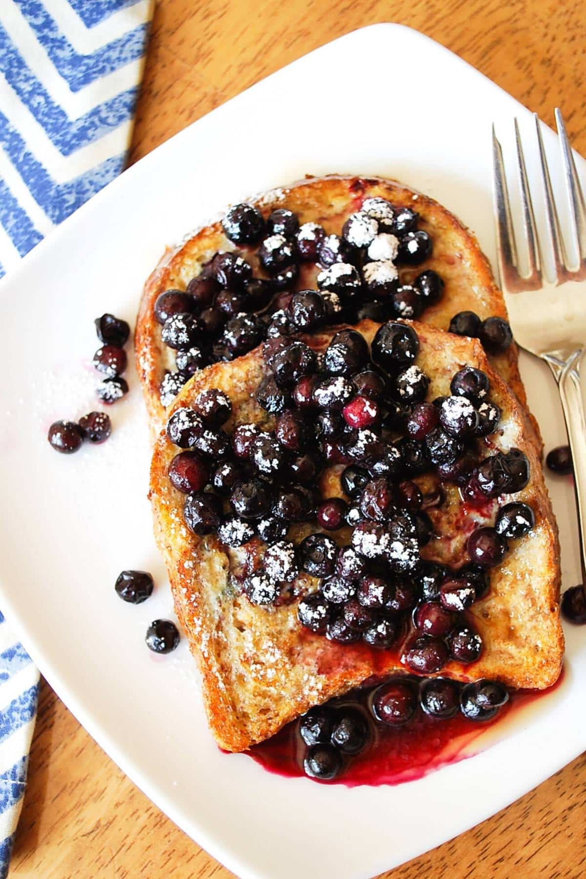 overhead photo of two slices of anabolic french toast on a plate topped with wild blueberries and powdered sugar