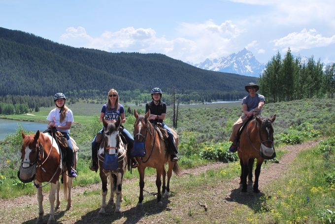 A group of people riding horseback with the Grand Tetons in the background