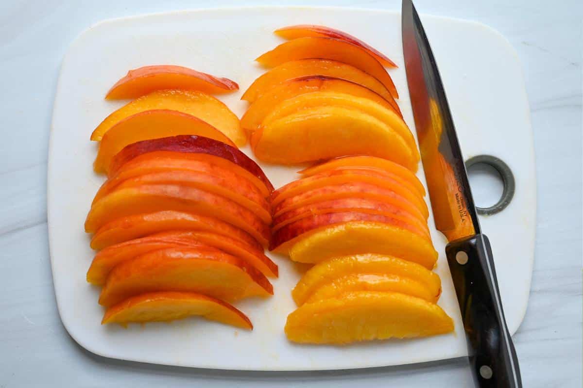 thinly sliced peaches on a cutting board with a knife