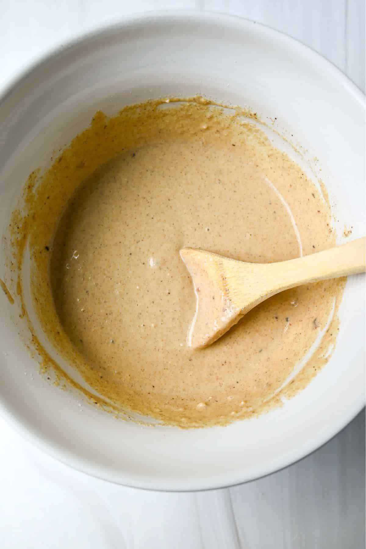 peach protein pancake batter mixed in a white bowl with a wood spoon