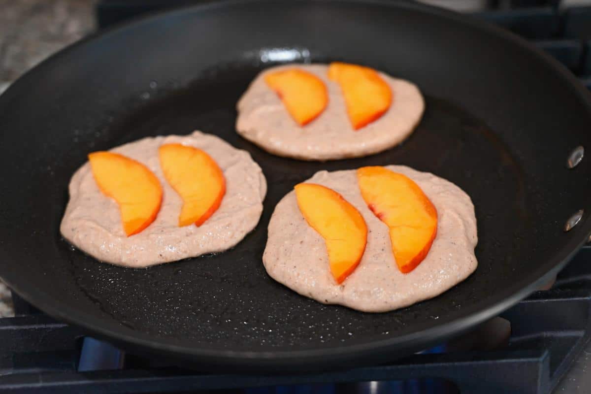 peach slices on top of pancake batter in a skillet