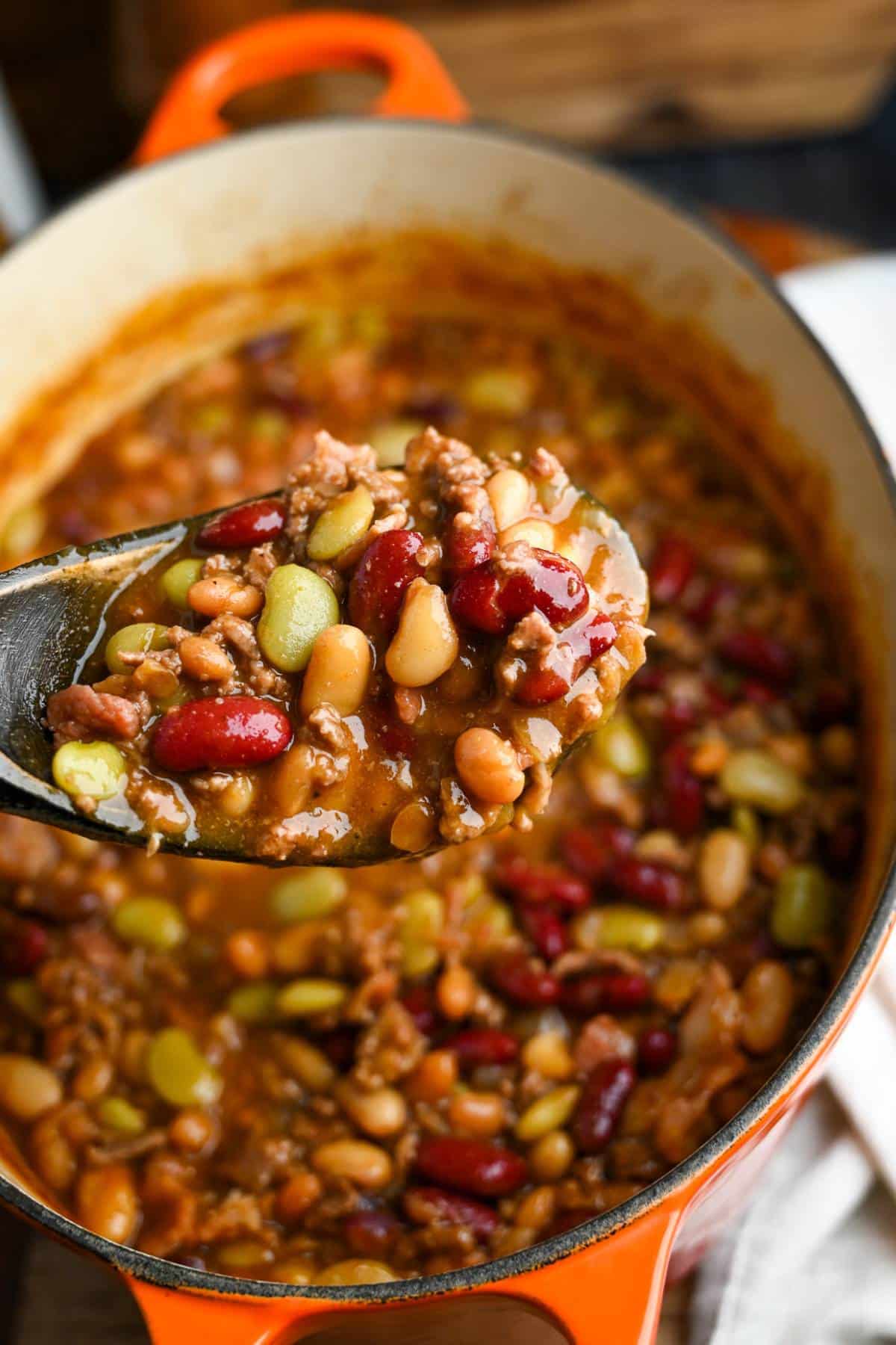 holding up a wooden ladle full of baked beans over a dutch oven with beans