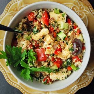 overhead photo of a chicken quinoa salad with fresh vegetables and olives and a sprig of parsley for garnish