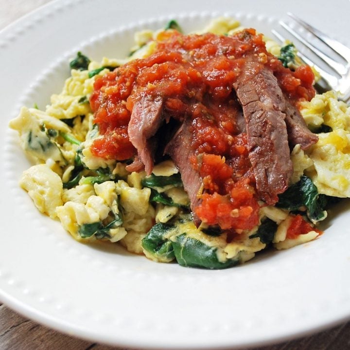 bowl of scrambled eggs with spinach topped with flank steak and salsa