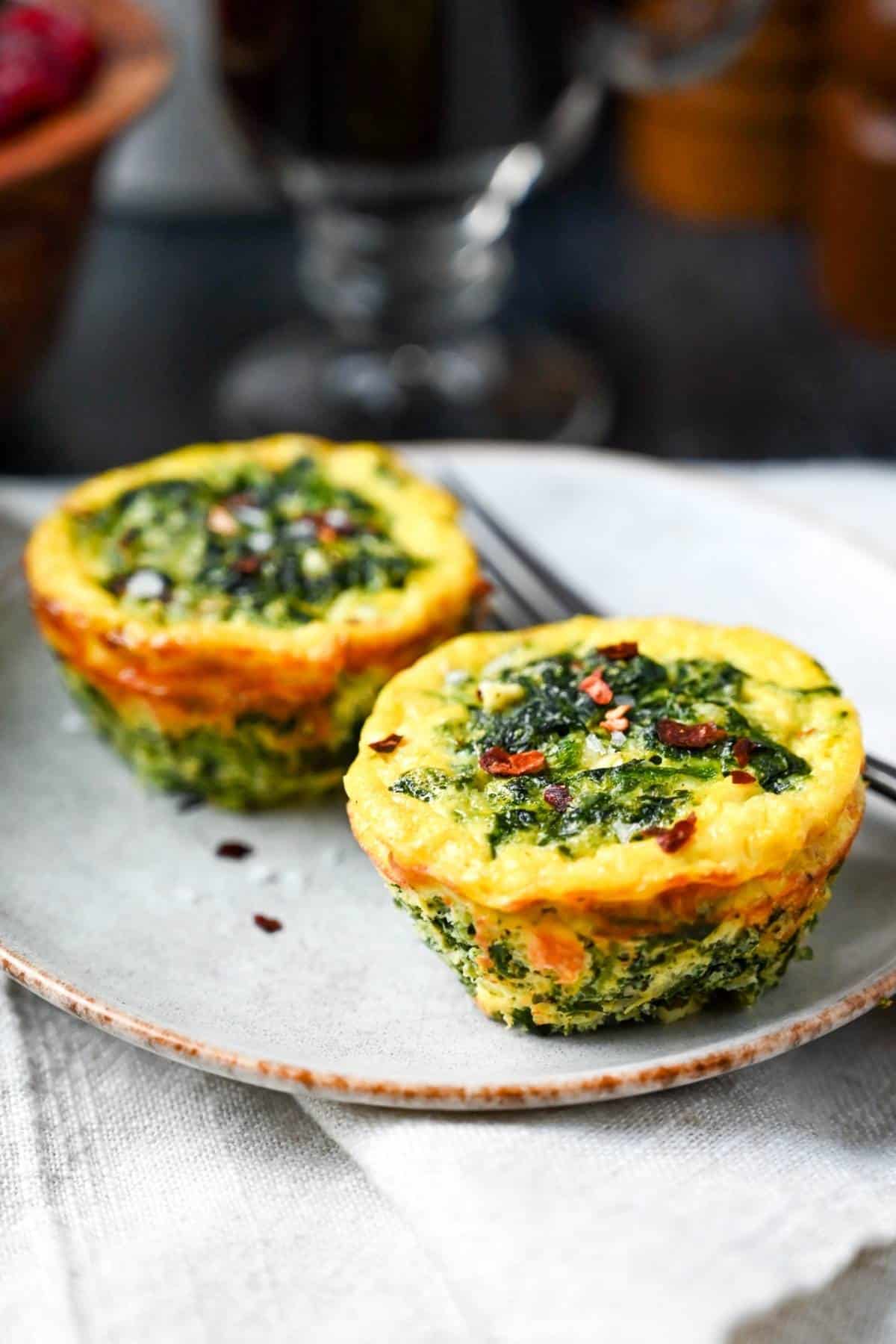 two spinach and cheese egg muffins on a plate with a fork