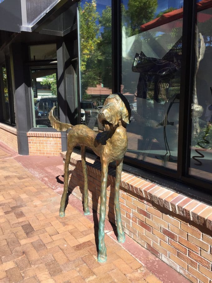 A dog statue on a sidewalk in front of a brick building