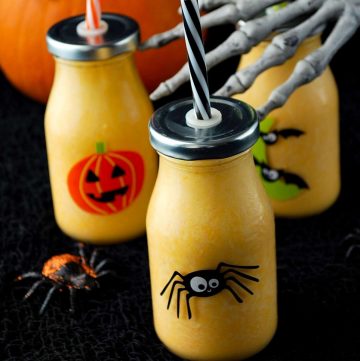 close up photo of halloween orange smoothies in Halloween glasses with lids and a straw