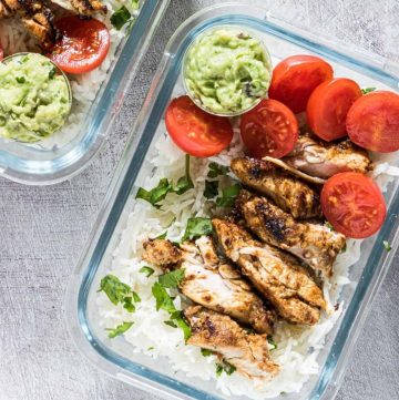 chicken and rice in two meal prep containers with sliced tomatoes