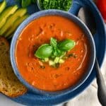 a bowl of gazpacho with basil, chives, cucumber, and olive oil on top