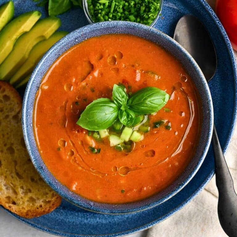 a bowl of gazpacho with basil, chives, cucumber, and olive oil on top