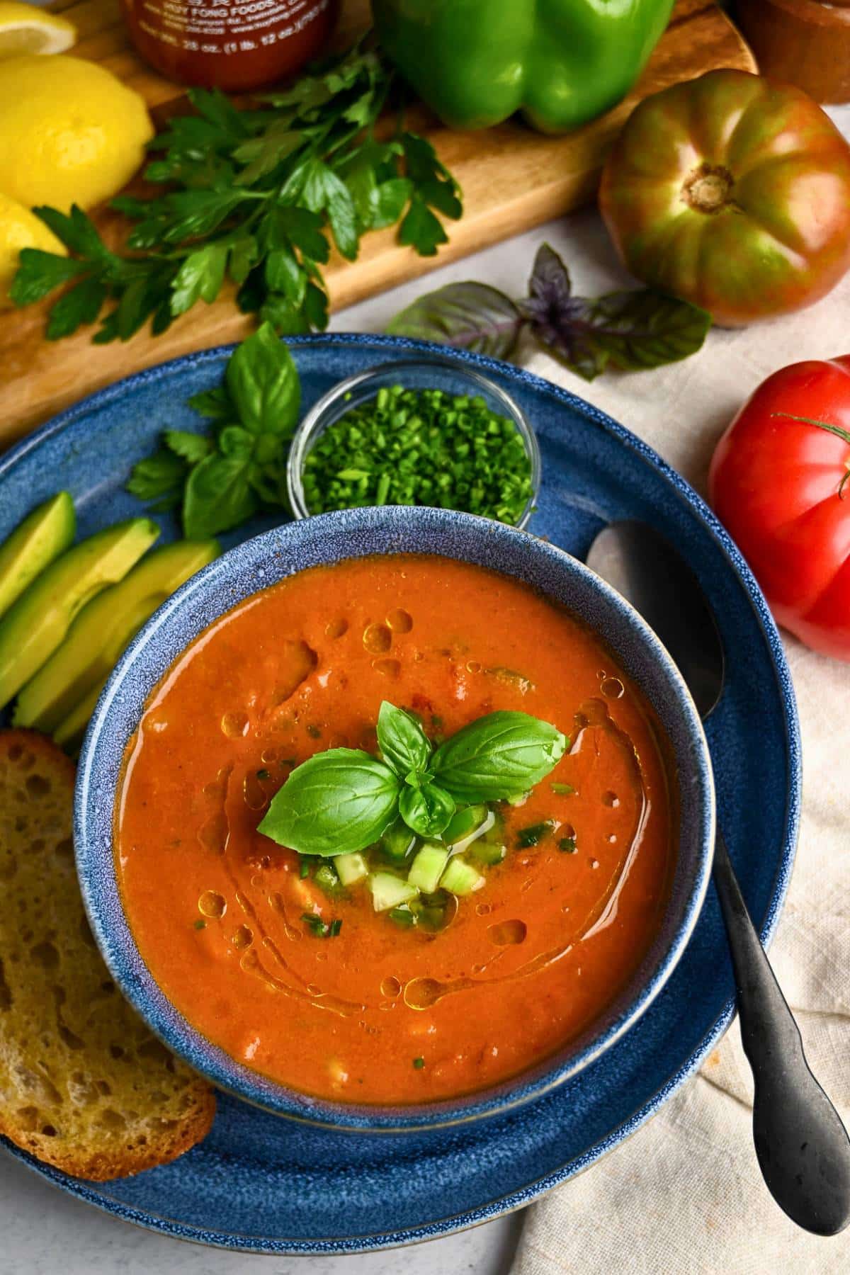 a bowl of spicy gazpacho soup with sliced avocado, and a toasted slice of sourdough on a plate