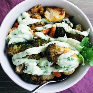 roasted broccoli, cauliflower, carrots, and grains in a bowl drizzled with a yogurt dressing and garnished with a sprig of parsley