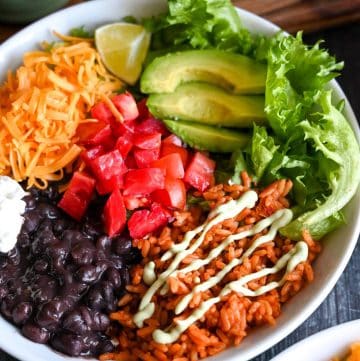 veggie bowl with rice, beans, tomatoes, cheese, avocado and sour cream with avocado dressing drizzle