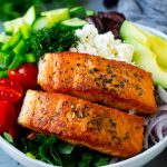 two slices of salmon in a bowl with Greek salad toppings