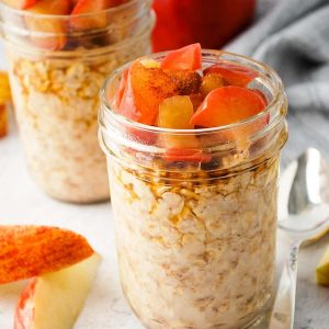 Apple pie oats in two mason jars topped with cooked apples and maple syrup